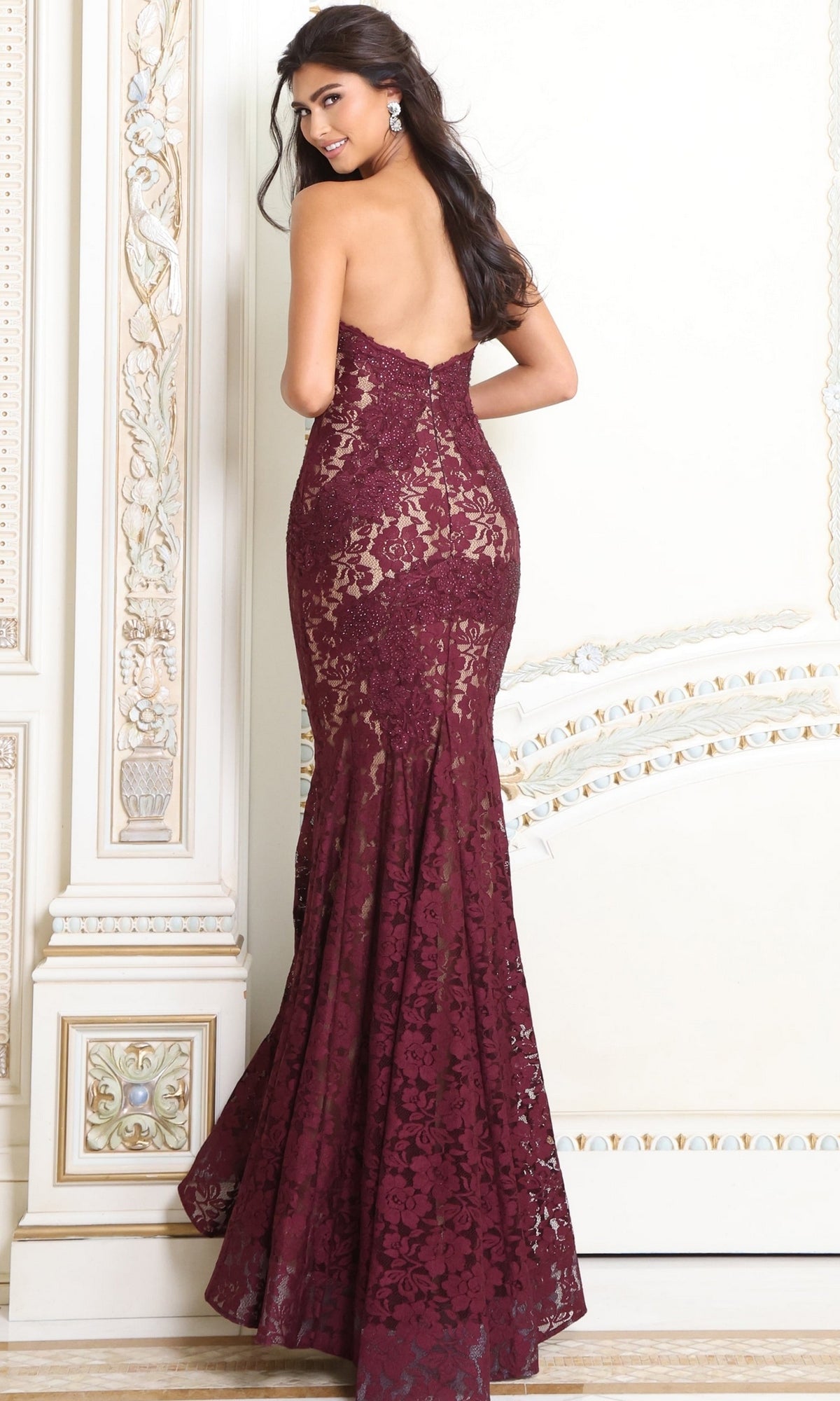 A person wearing a Strapless Long Lace Prom Dress; Jovani 37334, a backless, floor-length burgundy lace gown with a mermaid silhouette and a sweetheart neckline.